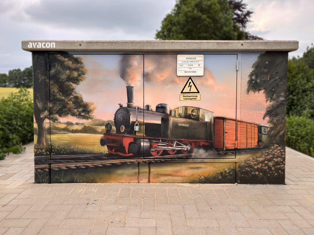 Detailliertes Wandgemälde der Dampflokomotive Bruchhausen auf der Avacon Trafostation in Dille zur goldenen Stunde